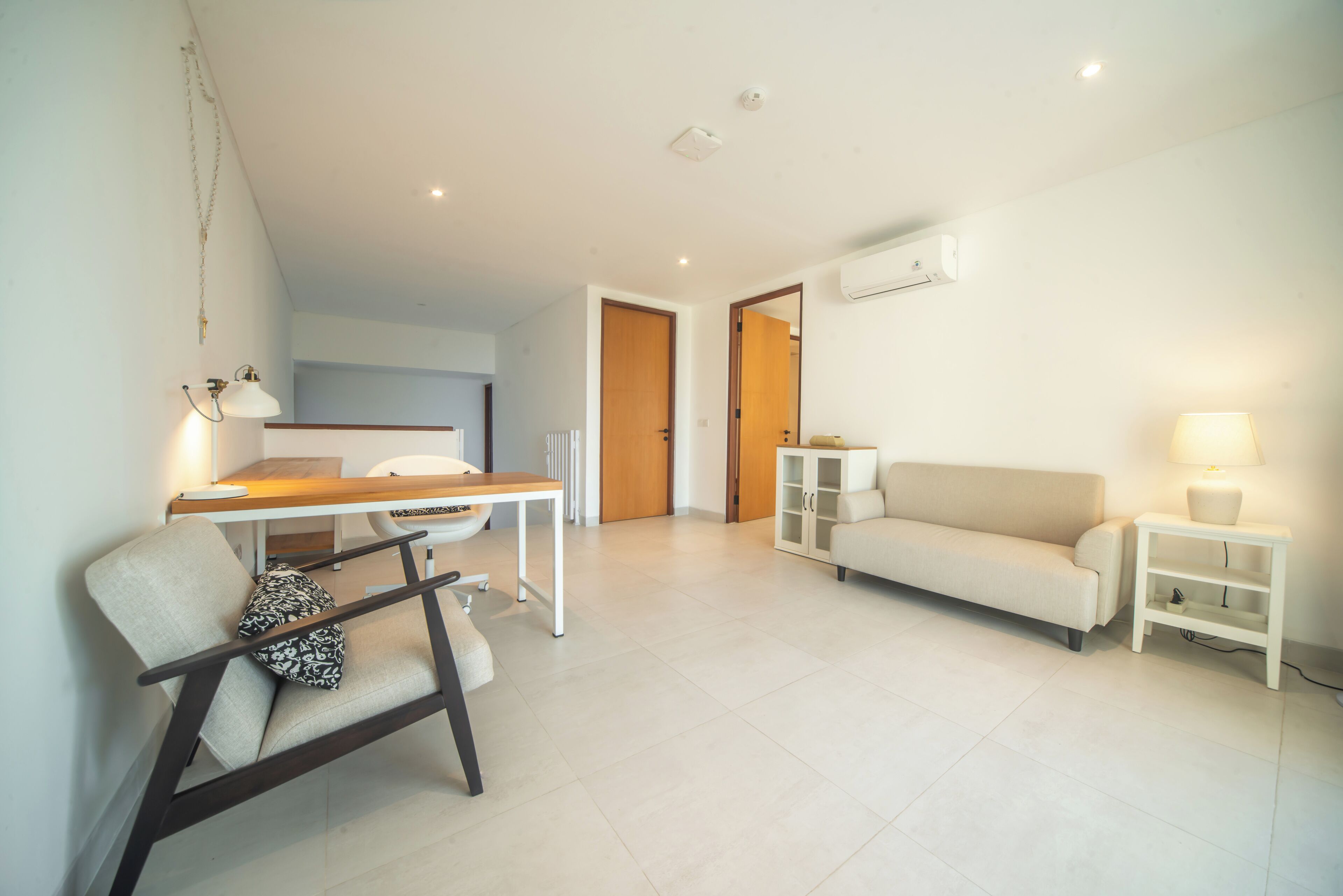A modern living room with a sofa, a dining table, and a chair. There is a kitchen area visible through an open door.