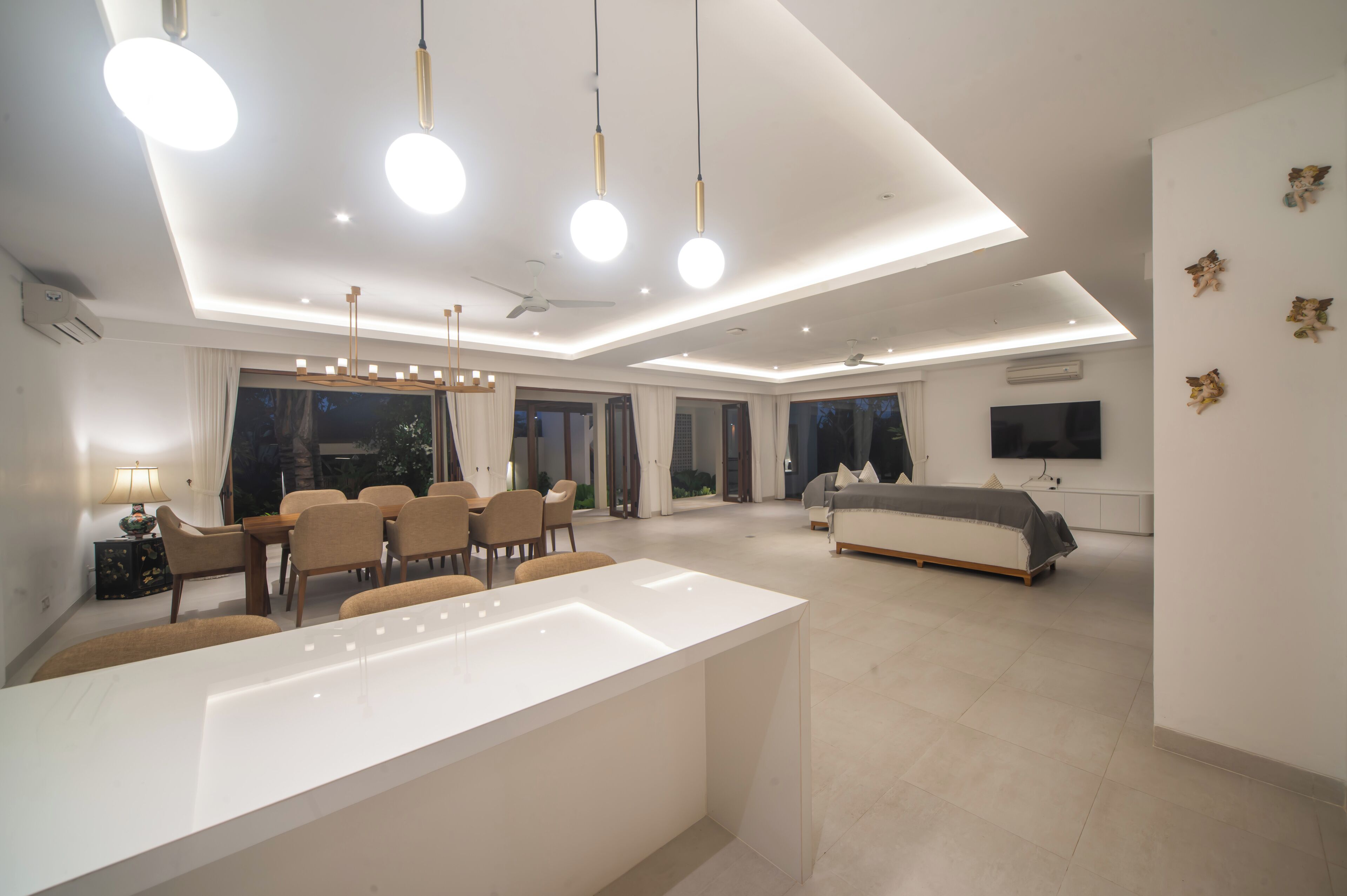 Una sala de estar moderna con una isla blanca central, un comedor con sillas, un sofá y un televisor montado en la pared.