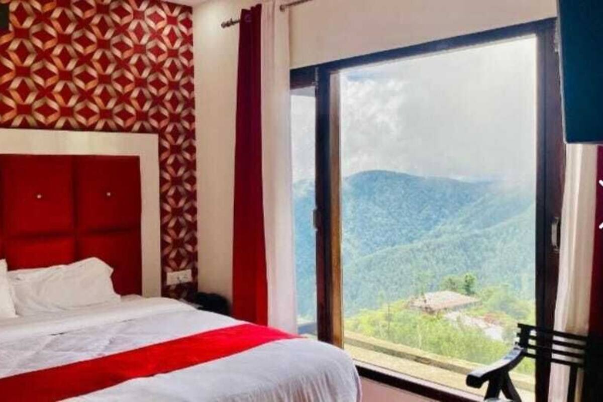 Ein Hotelzimmer mit einem großen Bett, einer Wand mit rotem Muster und Blick auf eine Berglandschaft durch ein großes Fenster.