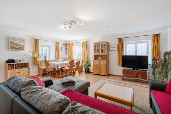 A living room with a sofa, a coffee table, a TV, and a dining area with a table and chairs.