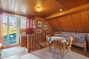 A wooden interior with a dining area, a sofa, and a staircase leading outside.