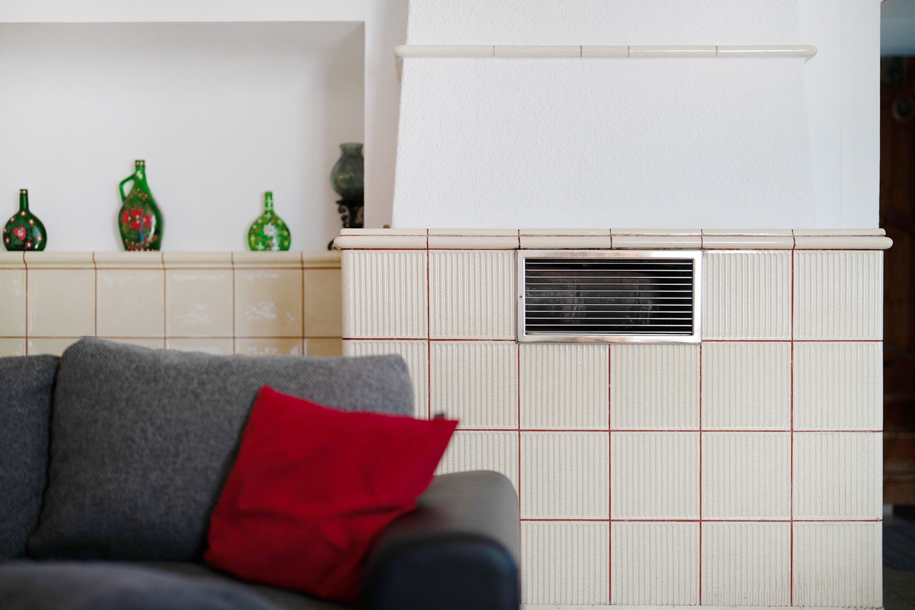 Una sala de estar con un sofá, un cojín rojo y una pared de azulejos con botellas decorativas.