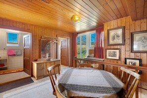 A wooden cabin interior with a dining table, chairs, a wooden cabinet, a mirror, and framed pictures on the walls.
