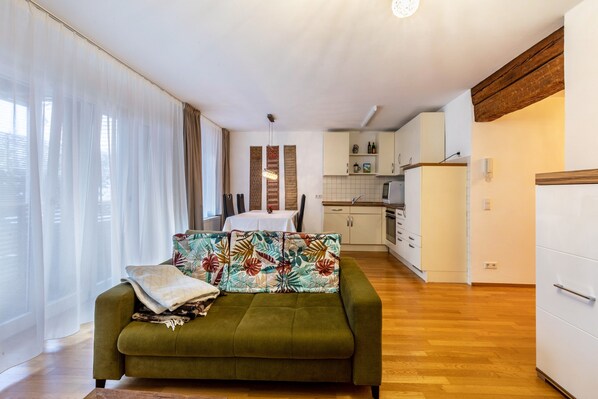 A living room with a sofa, a dining table, and a kitchen in the background.