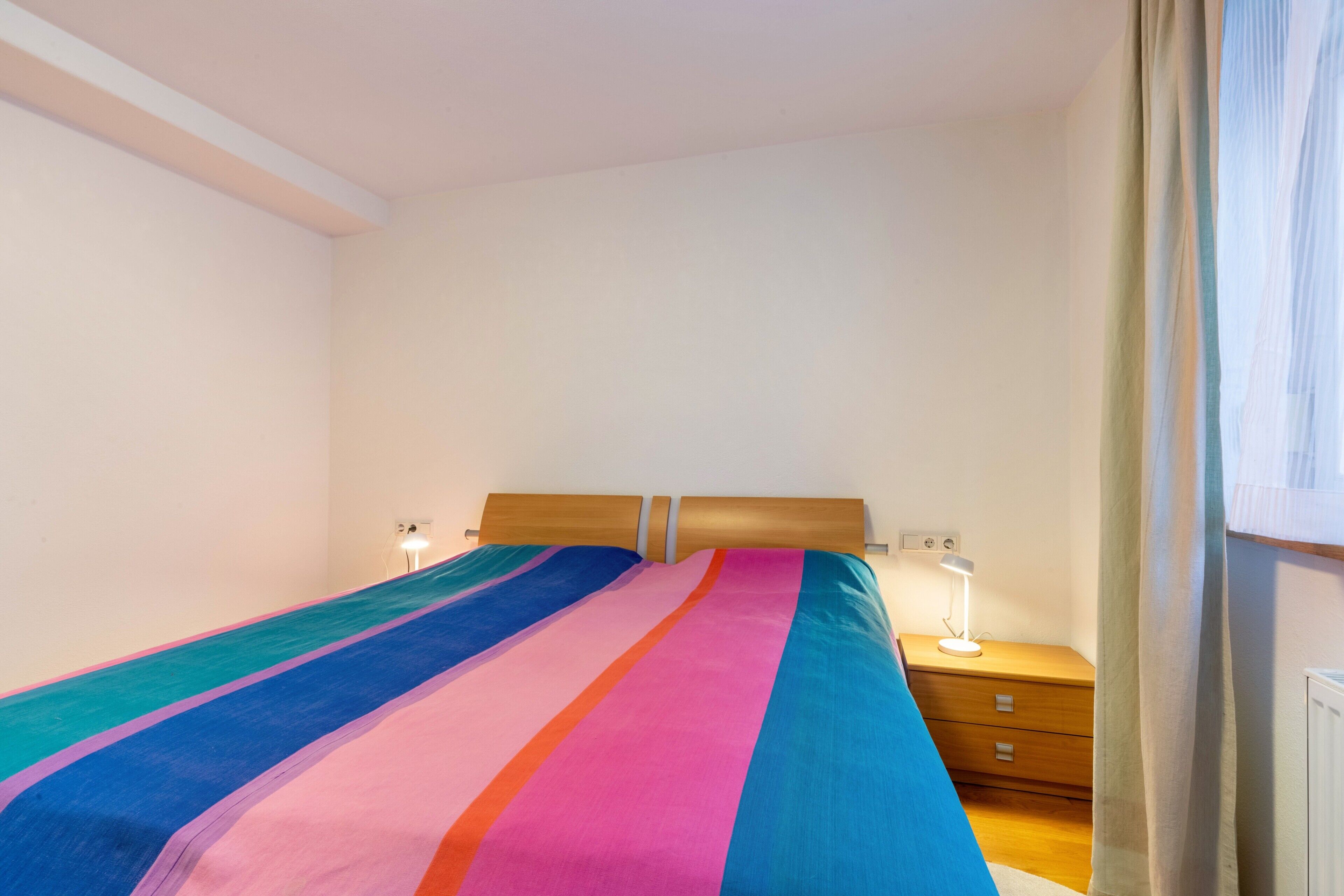 A bedroom with a bed, bedside tables, a lamp, and a window with curtains.