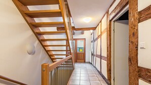 Un escalier en bois, doté d’une rampe, mène à une porte située au bout d’un couloir dont le sol est recouvert de carreaux.