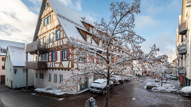 Un bâtiment traditionnel à colombages, doté d’un toit à forte pente, situé dans une rue étroite, avec des voitures garées.