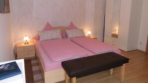 Une chambre à coucher avec un lit double, des tables de chevet avec des lampes, un banc, une armoire et un miroir.