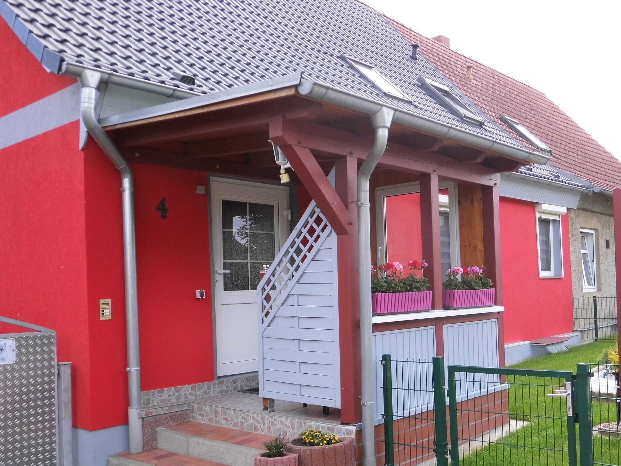 A red building with a white door, a staircase, and a small porch with flower boxes.