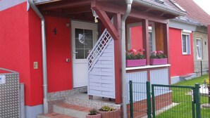 Un bâtiment rouge avec une porte blanche, un escalier et un petit porche agrémenté de jardinières.