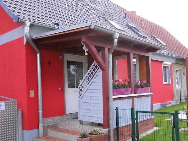 En röd byggnad med en vit dörr, en trappa och en liten veranda med blomlådor.