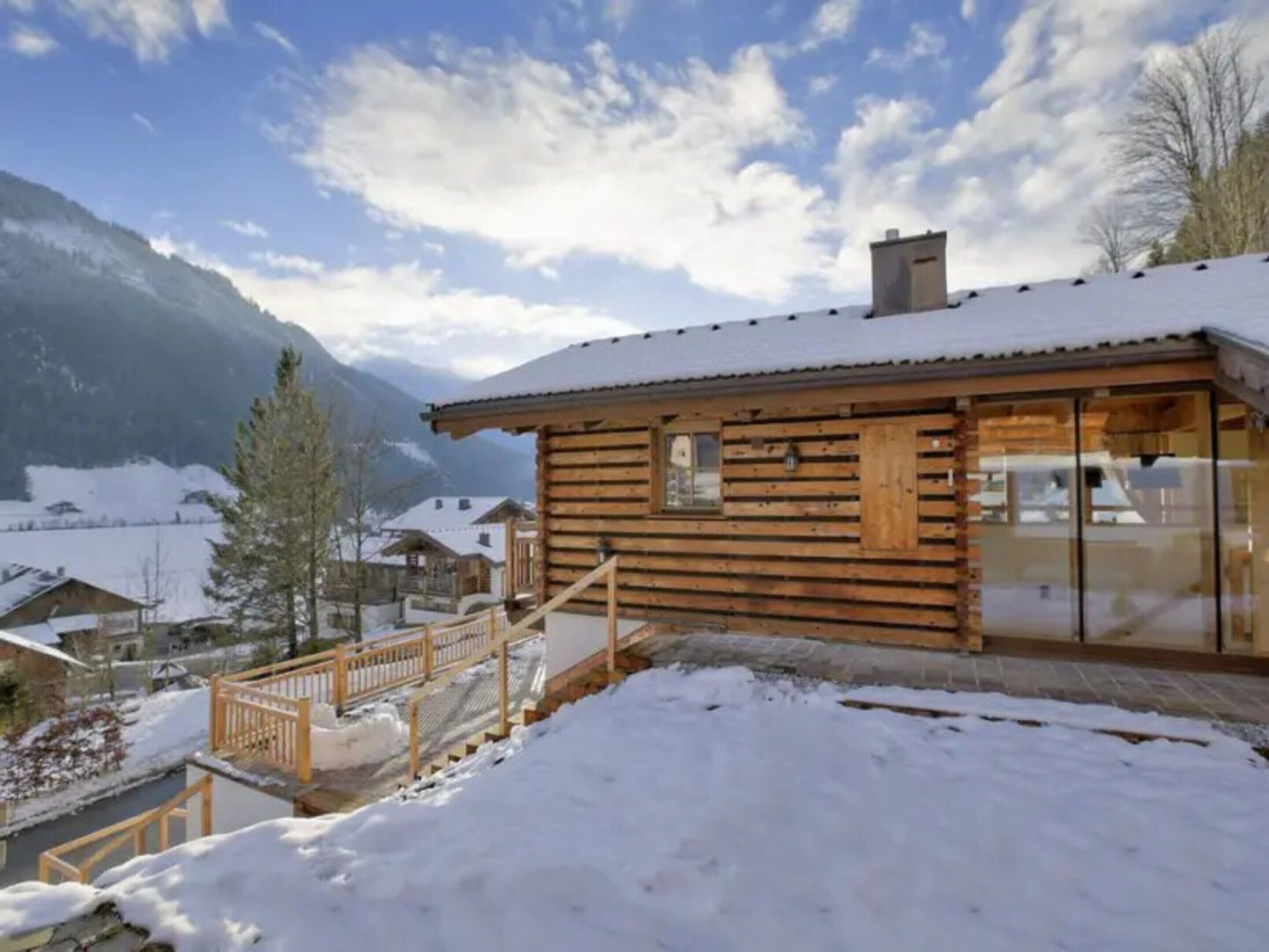 A wooden cabin with a balcony, surrounded by snow-covered mountains and clear skies.
