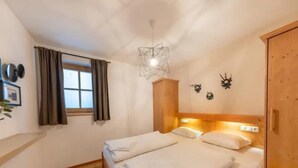 Une chambre à coucher avec un lit en bois, une fenêtre avec des rideaux, un luminaire fixé au mur et une armoire en bois.