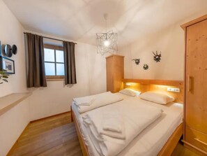 A bedroom with a wooden bed, a window with curtains, a wall-mounted light fixture, and a wooden wardrobe. - Schoneben Alpine Holiday Home (Wald im Pinzgau)