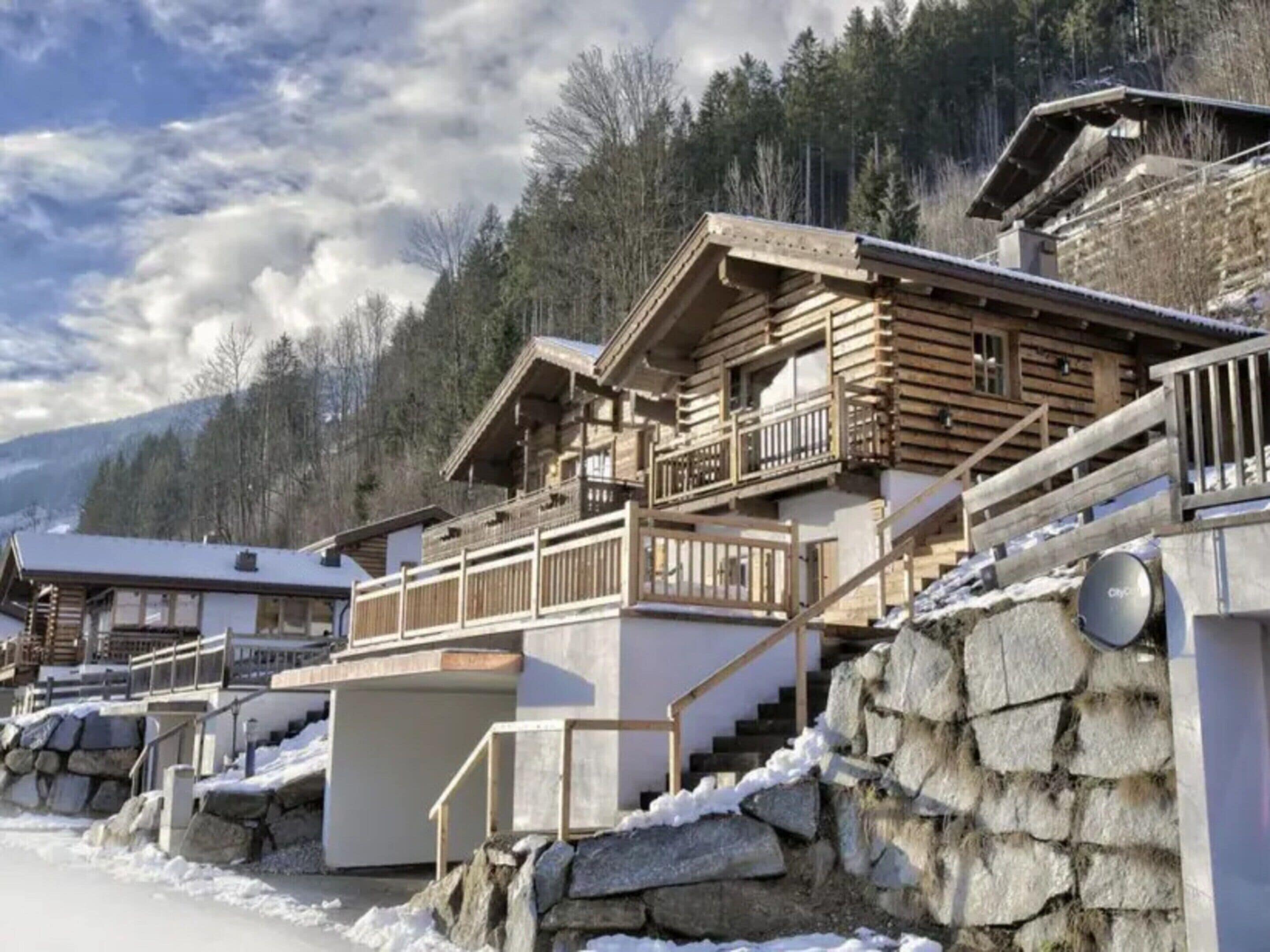 Un chalet en bois doté de plusieurs balcons, d’un escalier en pierre et surplombant un paysage montagneux.