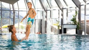 Une piscine intérieure avec des parois en verre transparent, donnant sur l’extérieur, et une personne debout sur les épaules d’une autre.