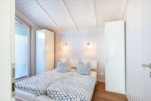 A bedroom with a bed, two wall-mounted lights, a wardrobe, and a door. - Apartment 'Aquamarin' with Private Terrace and Private Garden (Wesselburener Koog)