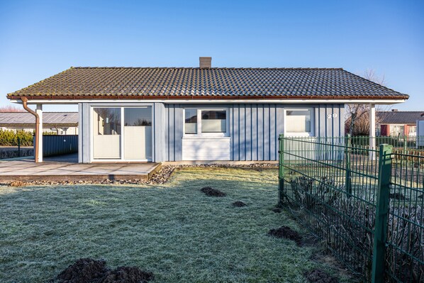 Ein Wohnhaus mit Ziegeldach, einer Veranda und einem umzäunten Garten.