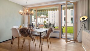 Ein Essbereich mit Tisch, Stühlen und einer Chandelier. Blick auf ein Gebäude und einen Balkon.