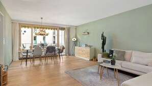Ein modernes Wohnzimmer mit Holzboden, einer Couch, einem Essbereich mit Stühlen, einem Tisch und einer Kakteenpflanze.