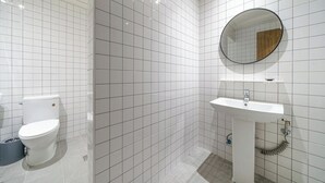 A bathroom with white tiled walls, a white sink, and a round mirror. - From H Dongbaek Hotel By Kwon Geoje Okpo (Geoje)