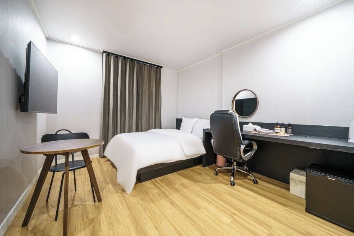 A hotel room with a bed, a desk, a chair, a television, and a small refrigerator.