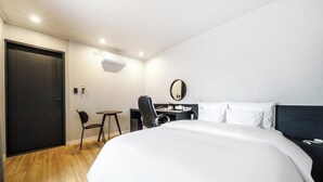 A hotel room with a large bed, a desk with a chair, a small table, and a mirror on the wall. - From H Dongbaek Hotel By Kwon Geoje Okpo (Geoje)