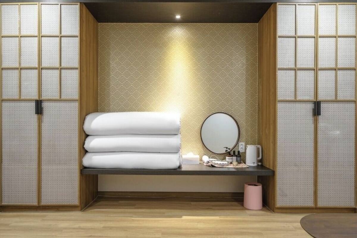 A room with a bed, a round mirror, a small table with toiletries, and a wall with a geometric pattern.