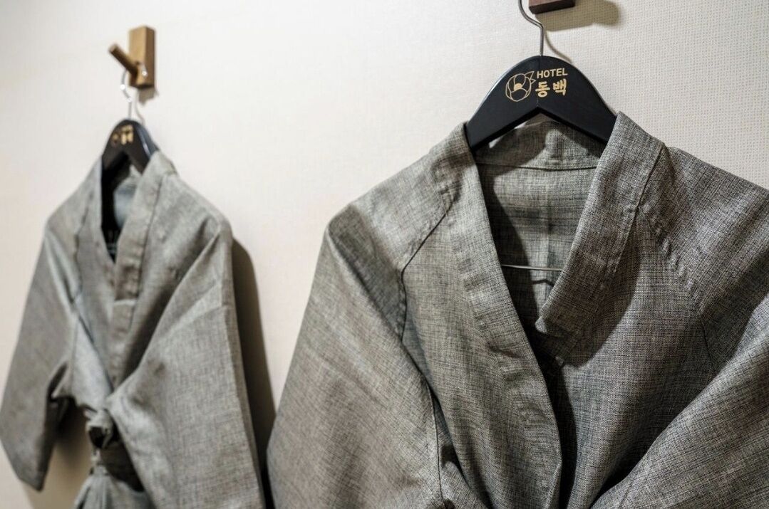Two grey robes hanging on black hangers with a hotel logo.