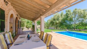 Un espacio de comedor al aire libre con piscina, terraza cubierta y paredes de piedra.