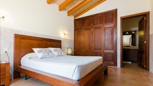 Un dormitorio con cama de madera, una mesita de noche, un armario y un baño visible a través de una puerta abierta.