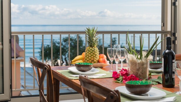 Ein Esstisch mit Blick auf den Ozean, eine Ananas und eine Weinflasche auf einem Balkon.