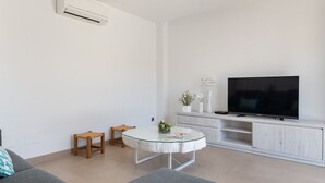 A modern living room with a glass-top coffee table, a flat-screen TV, a sofa, and a small wooden stool. - Ca Na Xisca 2 - Apartment In Can Picafort (Can Picafort, Illes Balears)