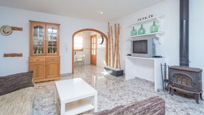 Una sala de estar con un sofá, una mesa de centro, un aparador de madera, un televisor, una chimenea y un estante con botellas verdes.