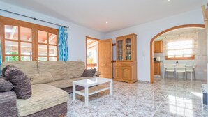 Una sala de estar con sofá, mesa de centro, armarios de madera y un comedor con mesa y sillas.