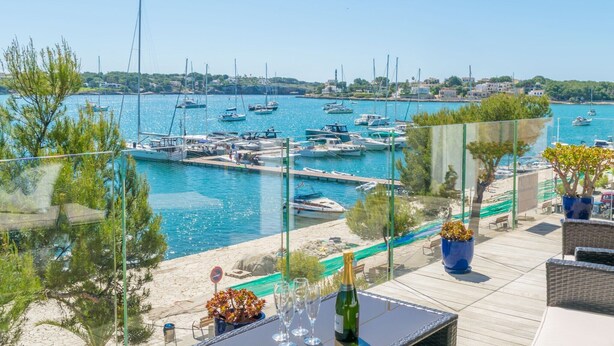 A marina with boats docked, a clear sky, and a view of the coastline. - Llevant - Apartment In Portocolom. Free Wifi (Portocolom, Illes Balears)