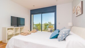 A bedroom with a bed, a TV, a large window, and a view of greenery. - Llevant - Apartment In Portocolom. Free Wifi (Portocolom, Illes Balears)