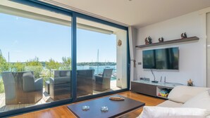 A modern living room with a large sliding glass door leading to an outdoor balcony, a flat-screen TV mounted on the wall, and a wooden coffee table. - Llevant - Apartment In Portocolom. Free Wifi (Portocolom, Illes Balears)