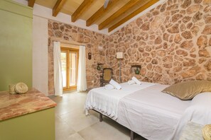 A bedroom with a stone wall, a bed with white linens, a wooden ceiling, and a green wall.