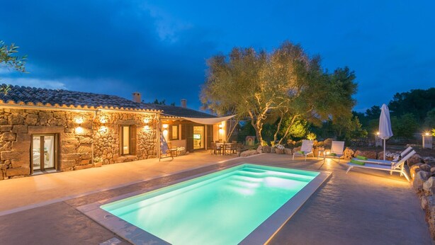 A stone building with a swimming pool, outdoor seating, and trees.