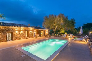 A stone building with a swimming pool, outdoor seating, and trees.