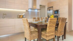 A modern kitchen with wooden cabinets, a stainless steel range hood, and a dining area with a dark wooden table and wicker chairs.