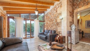 A spacious living area with a stone wall, wooden ceiling beams, a sofa, a coffee table, and a fireplace. - Cas Mostatxet (sencelles) - Villa With Pool (Sencelles, Illes Balears)