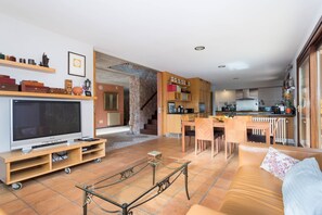 A modern living room with a TV, sofa, and coffee table. There is a kitchen area with a dining table and chairs. - Can Toni Gat - Villa With Private Pool In Bunyola (Bunyola, Illes Balears)
