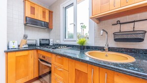 Une cuisine avec des meubles de rangement en bois, un plan de travail noir, un évier, une cuisinière et une fenêtre.