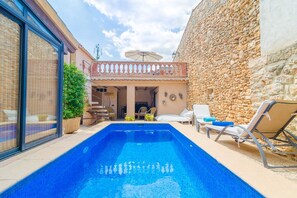 Ein Schwimmbecken mit Liegestühlen, einer Steinmauer und einer überdachten Terrasse.