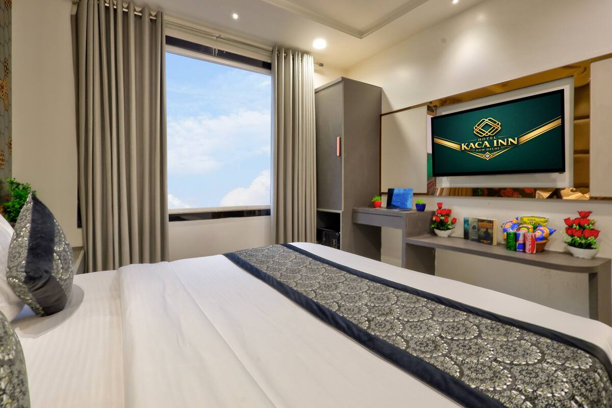 A hotel room with a bed, curtains, a television, a desk with a mirror, and a window with a view.