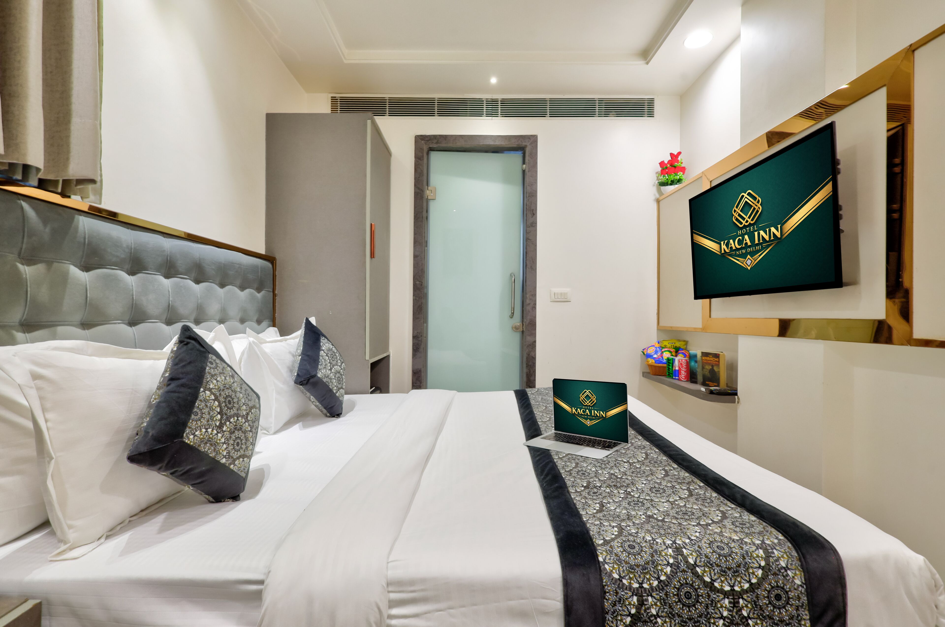 A hotel room with a bed, a television, a laptop, and a door.