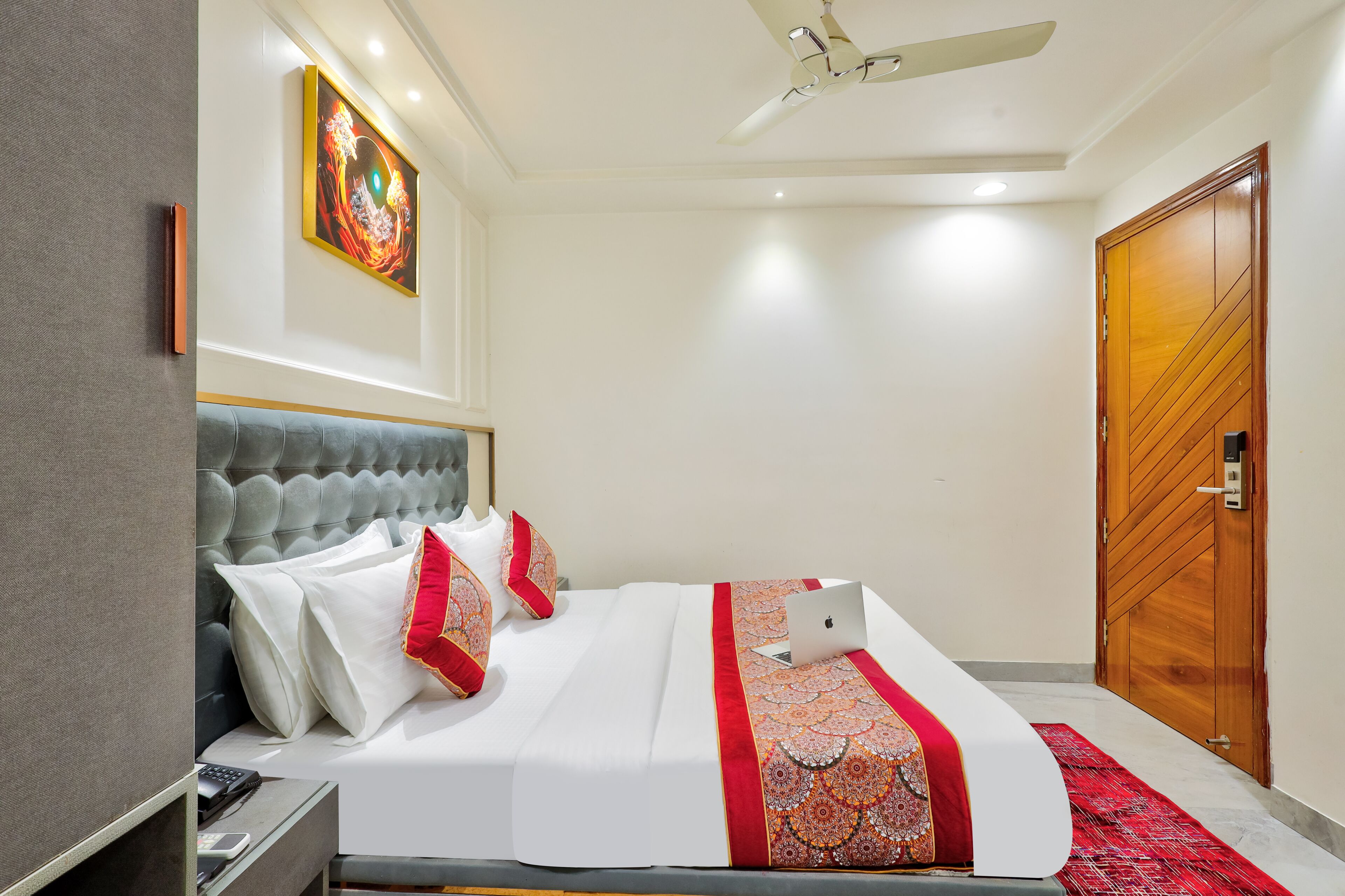 Une chambre d’hôtel bien rangée, avec un lit, un bureau, une chaise, un ventilateur de plafond et une porte.