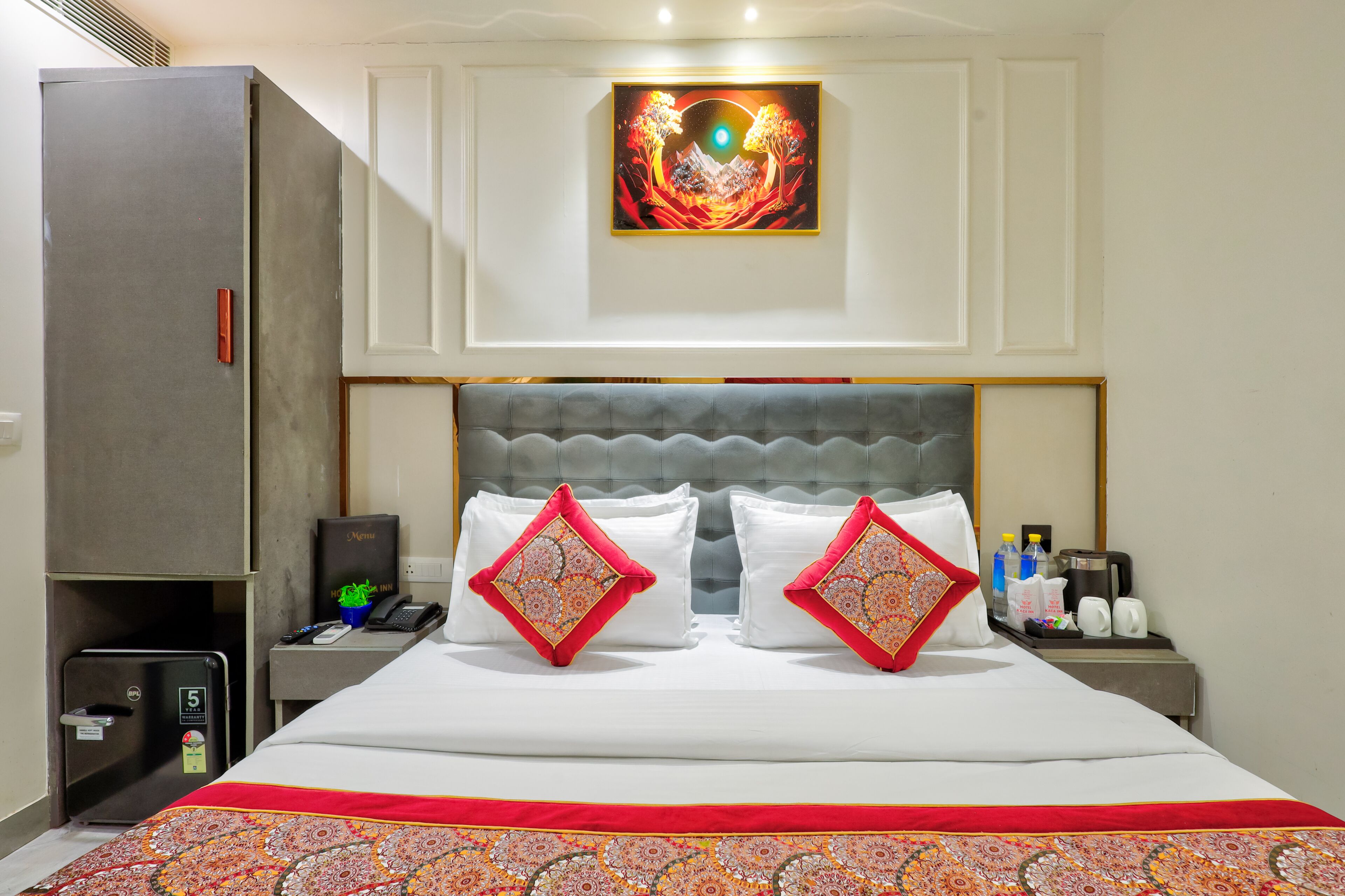 Une chambre d’hôtel avec un lit, une table de chevet, un minibar et un tableau au mur.